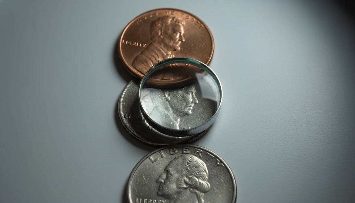 Close-up coins under a magnifying glass highlighting the small areas where dates and mint marks appear.